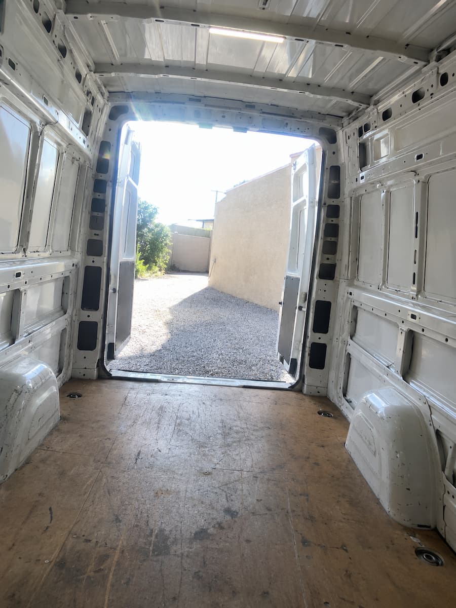 Inside the empty cargo bay, looking back through the open rear doors onto a gravel driveway.