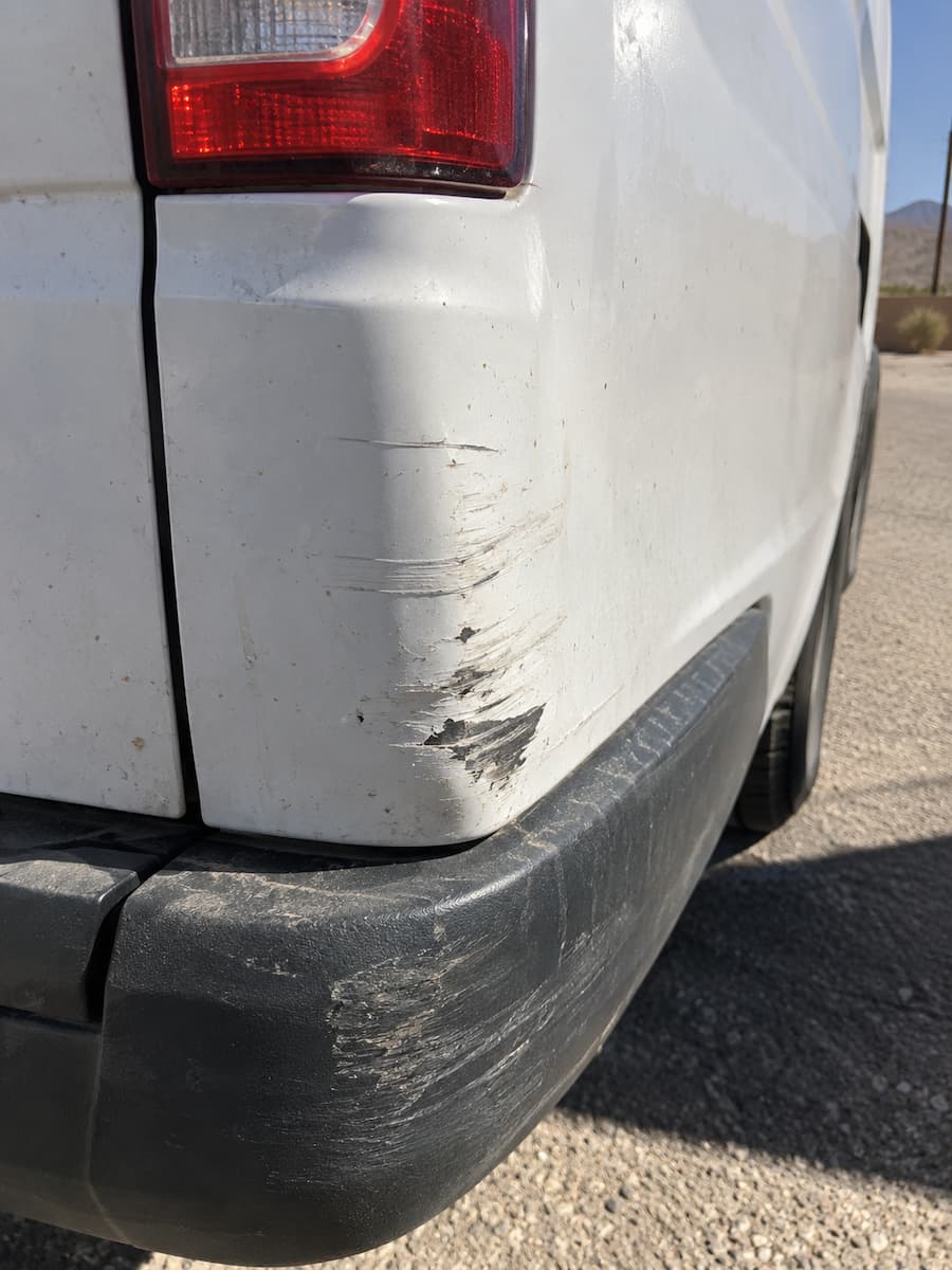 Scraped paint and gouged bumper on the rear corner of the van.